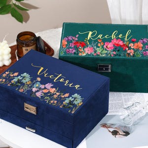 May include: Two velvet jewelry boxes, one navy blue and one emerald green, are displayed. Both boxes feature floral designs and personalized names in gold script. The navy box has the name "Victoria", while the green box says "Rachel".