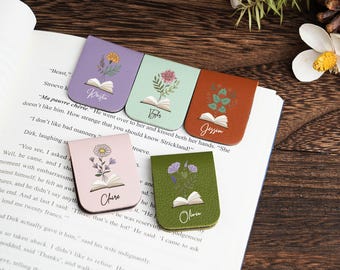 May include: Five leather bookmarks with floral designs and names. Each bookmark is a different colour: purple, mint green, orange, pink, and olive green. The bookmarks are on an open book.