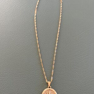 Pode incluir: Um colar de corrente de ouro com um pingente de b&uacute;ssola. A b&uacute;ssola &eacute; redonda e tem um centro preto com uma estrela dourada.
