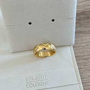 Könnte beinhalten: Ein goldfarbener Ring mit einem Steppmuster. Der Ring wird auf einer weißen Oberfläche mit dem Text "STILECHT COLOGNE" präsentiert. Es ist ein Schmuckstück.