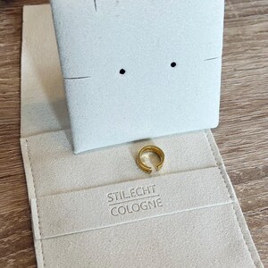 May include: A white velvet jewelry box with a gold ring inside. The box has the text "STIL.ECHT COLOGNE" printed on the inside.