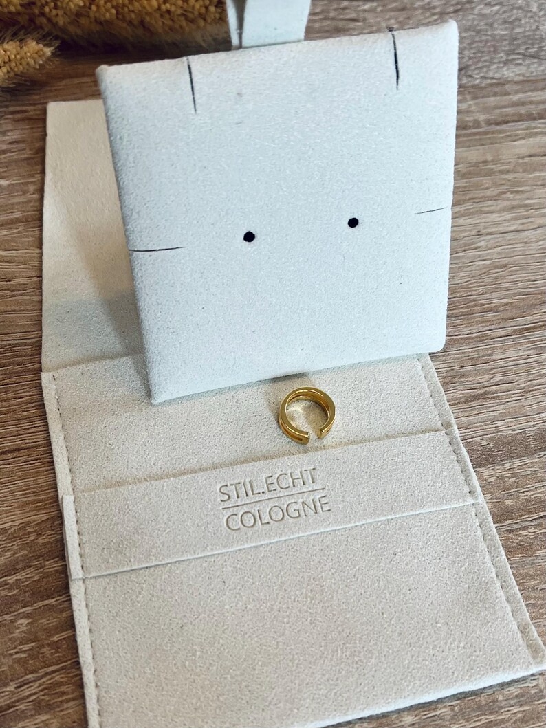 May include: A white velvet jewelry box with a gold ring inside. The box has the text "STIL.ECHT COLOGNE" printed on the inside.