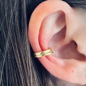 May include: Gold ear cuff jewelry. The cuff is a simple, thin band that wraps around the upper part of the ear.
