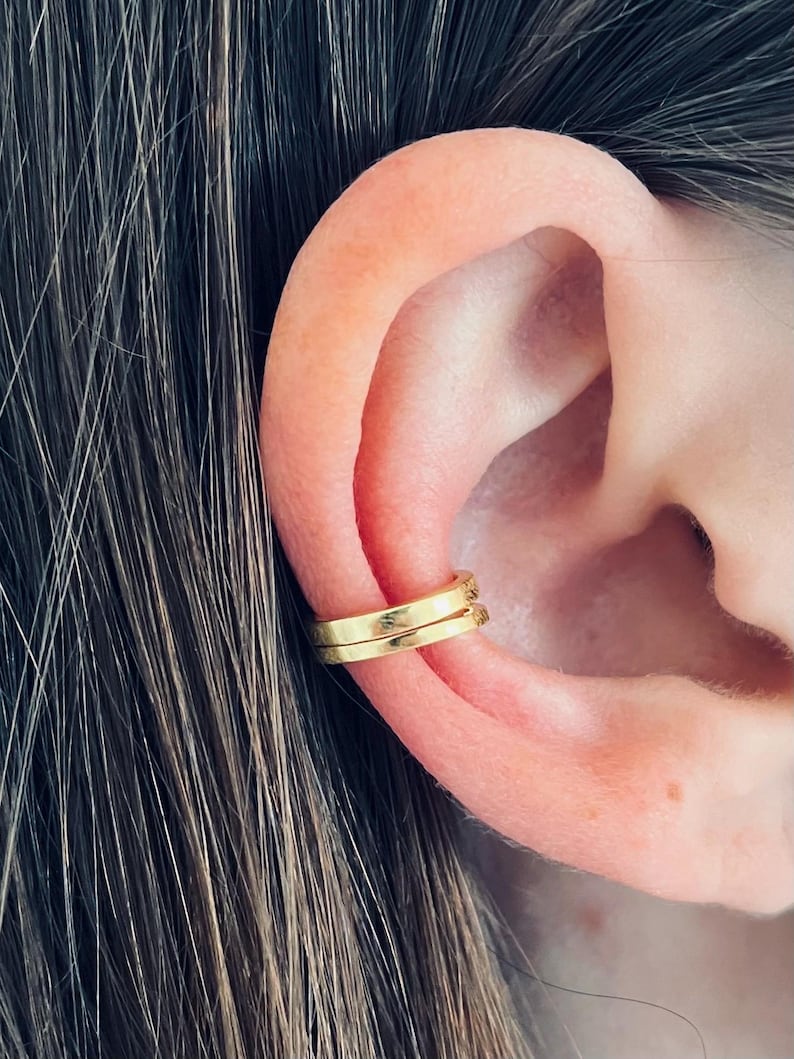 May include: Gold ear cuff jewelry. The cuff is a simple, thin band that wraps around the upper part of the ear.