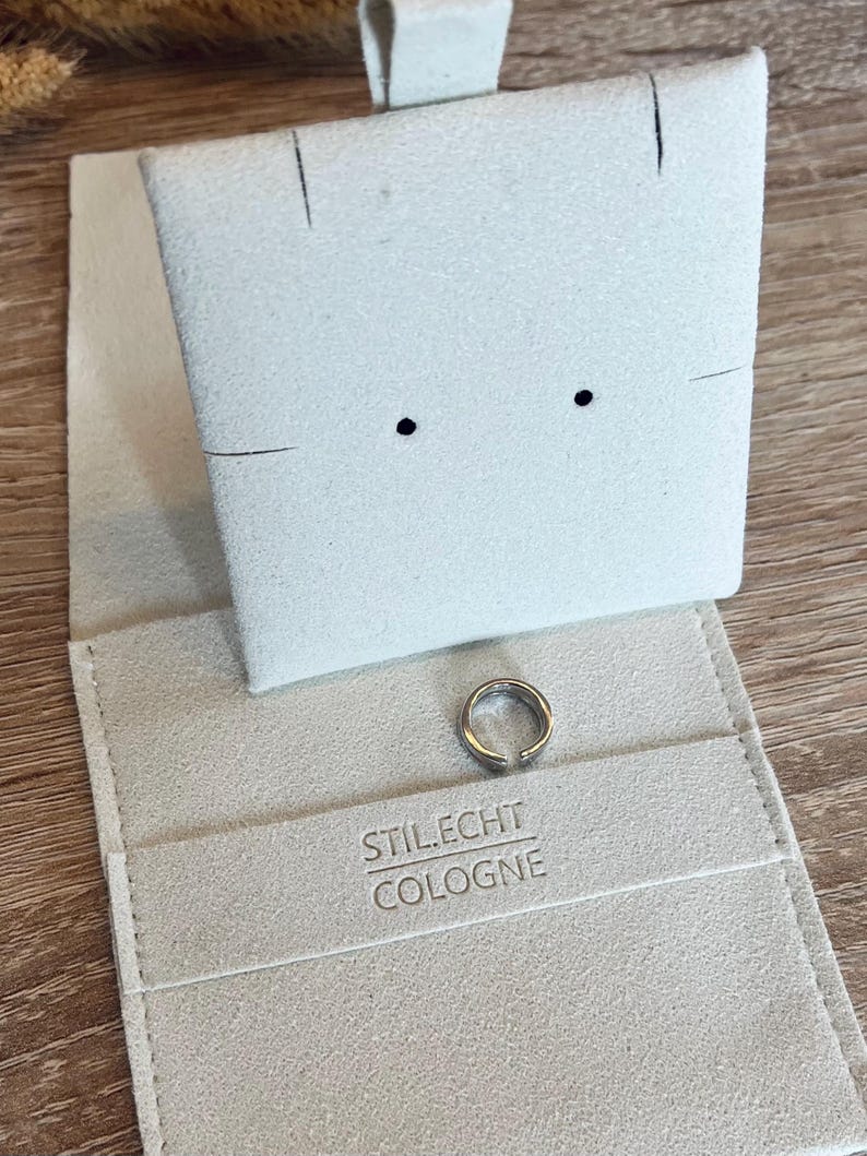 May include: A white felt jewelry box with a silver ring inside. The box has the text "STIL.ECHT COLOGNE" printed on the inside.