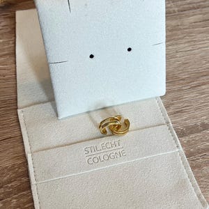 May include: A pair of gold hoop earrings in a white velvet jewelry box with the text "STILECHT COLOGNE" printed on the inside.