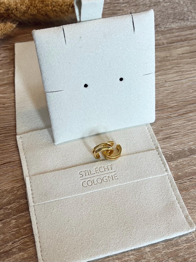 May include: A pair of gold hoop earrings in a white velvet jewelry box with the text "STILECHT COLOGNE" printed on the inside.