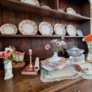 Victorian-style dresser display featuring antique Crown Derby Imari china, covered vegetable tureens, gravy boat, decorative plates, trailing ivy, garden flowers and old books creating a classic heritage interior vignette.