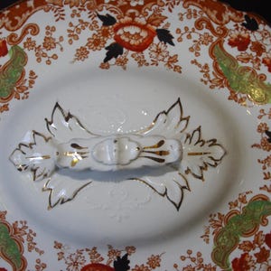 Close up from top of Antique W. Adams Crown Derby Imari Style lidded serving dish with white base with an orange, green, and black floral pattern.