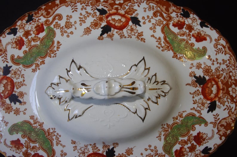 Close up from top of Antique W. Adams Crown Derby Imari Style lidded serving dish with white base with an orange, green, and black floral pattern.