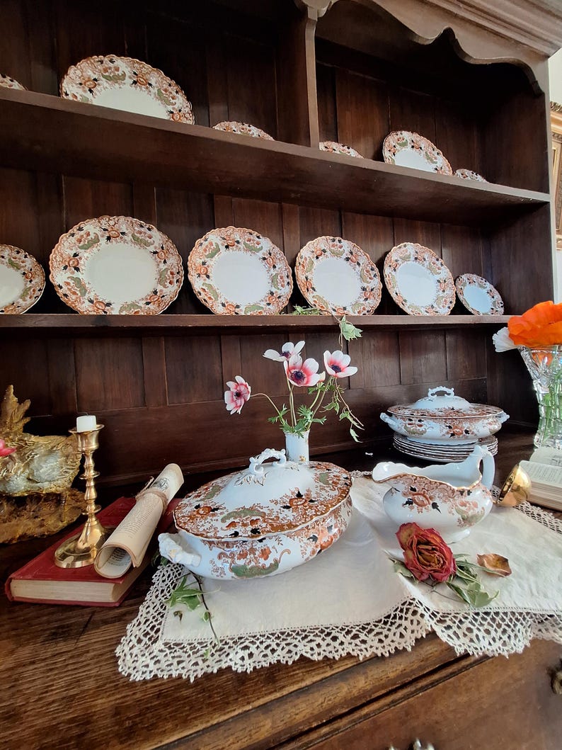 Large antique Crown Derby Imari china set displayed on an oak Welsh dresser featuring dinner plates, side plates, covered tureens, gravy boat, brass serving spoon and fresh garden flowers in a traditional English dining room setting.