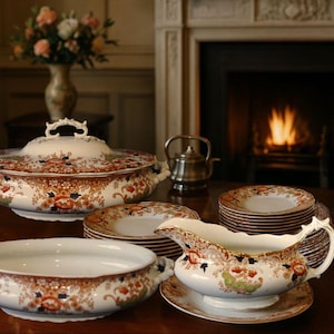 Antique W. Adams Crown Derby style dinner service, c.1900, displayed on a polished wooden table before a glowing Victorian fireplace. The 21-piece set includes two tureens, a gravy boat, and stacked dinner plates with rich floral decoration and gilt detail.