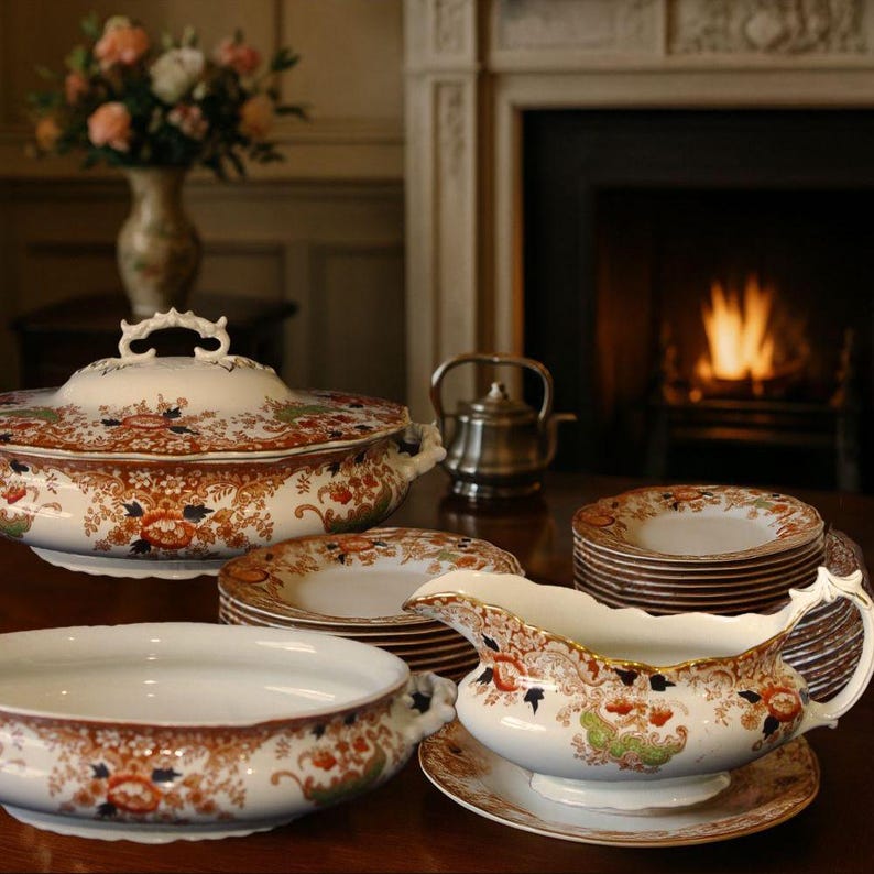 Antique W. Adams Crown Derby style dinner service, c.1900, displayed on a polished wooden table before a glowing Victorian fireplace. The 21-piece set includes two tureens, a gravy boat, and stacked dinner plates with rich floral decoration and gilt detail.