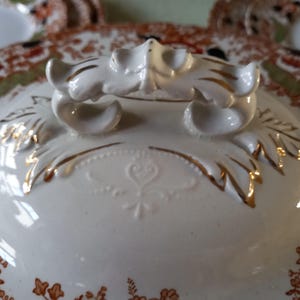 Close up from top of Antique W. Adams Crown Derby Imari Style lidded serving dish with white base with an orange, green, and black floral pattern.