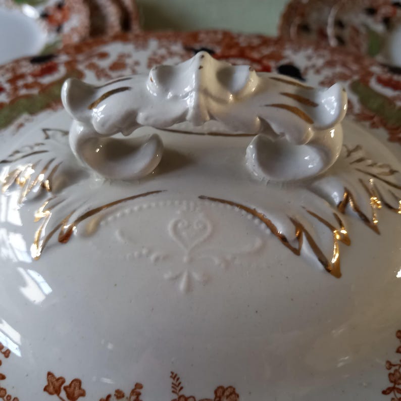 Close up from top of Antique W. Adams Crown Derby Imari Style lidded serving dish with white base with an orange, green, and black floral pattern.