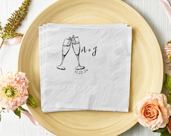 May include: White paper napkins with a black illustration of two champagne glasses clinking. The text "A + J" and "1.22.24" is printed below the glasses.
