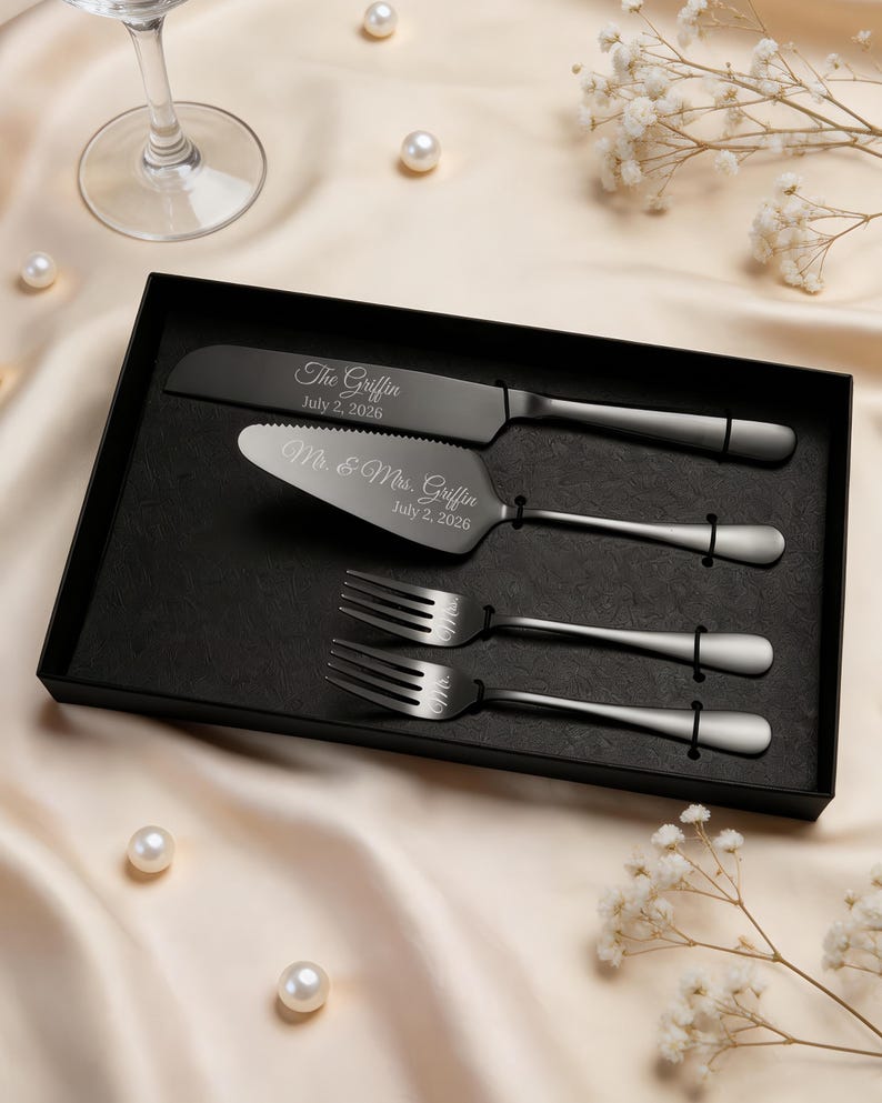 May include: A matte black cake serving set in a black presentation box, including a knife and server engraved with "The Griffin July 2, 2026" and "Mr. & Mrs. Griffin July 2, 2026," plus two matching forks engraved with "Mr." and "Mrs."