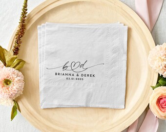 May include: White paper napkins with a black script font that reads "b&d" with a heart in the middle. The text below reads "Brianna & Derek 03.21.2025".