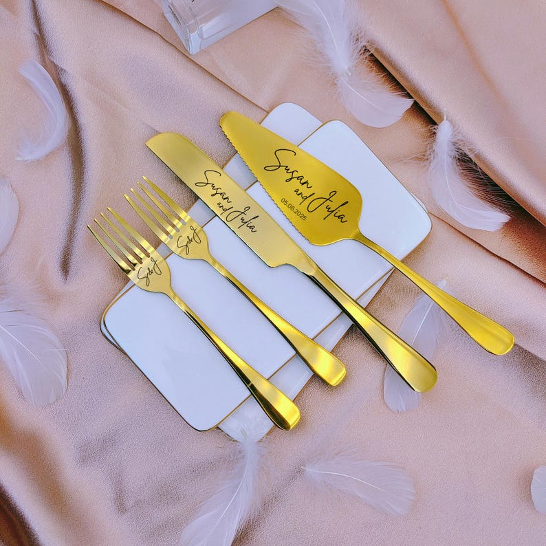 May include: A set of gold-toned stainless steel cutlery including two forks, a knife, and a cake server. The knife and server are engraved with the text Susan and Julia, and the forks are engraved with S&J. The server also features the date 05.08.2025.