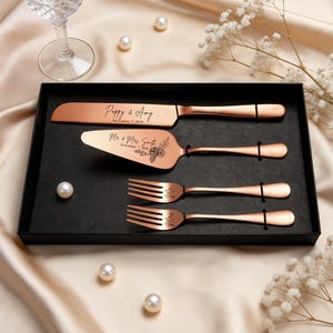 May include: A rose gold cake serving set in a black box, including a knife, a cake server, and two forks. The knife is engraved with Poppy & Amy November 7, 2026, and the server features Mr & Mrs Smith November 7, 2026, with a floral design.