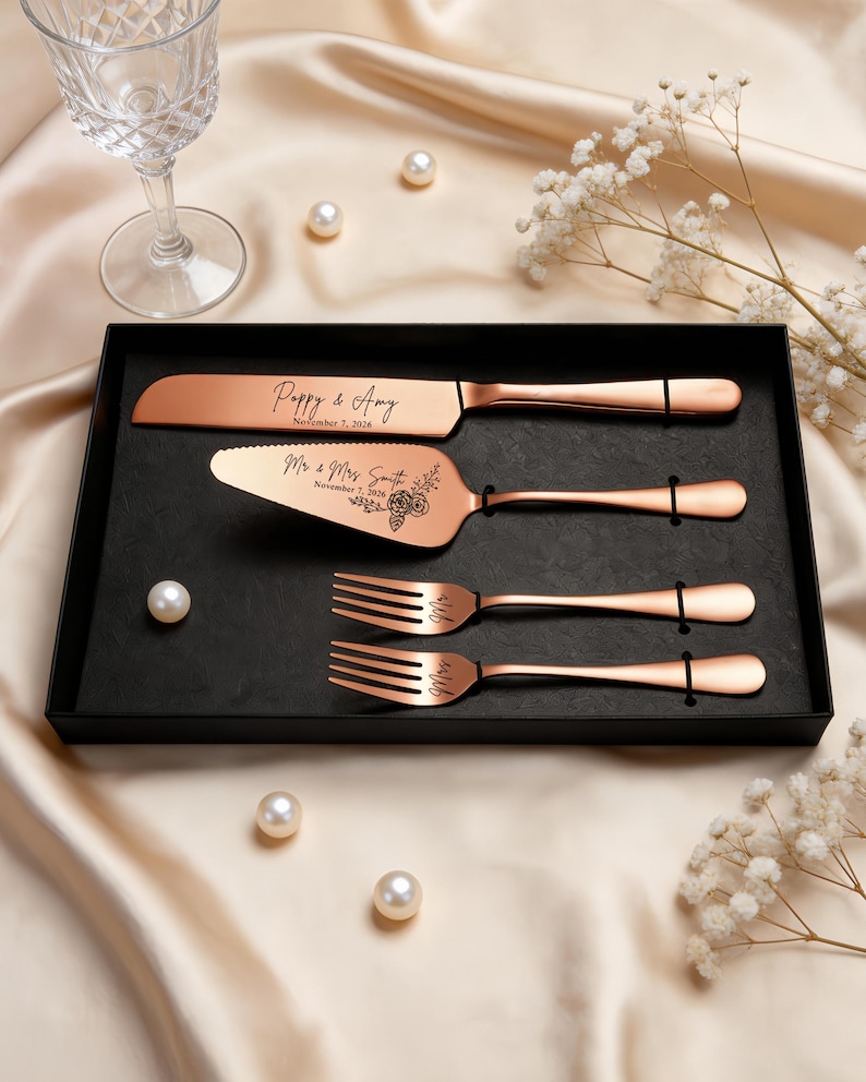 May include: A rose gold cake serving set in a black box, including a knife, a cake server, and two forks. The knife is engraved with Poppy & Amy November 7, 2026, and the server features Mr & Mrs Smith November 7, 2026, with a floral design.