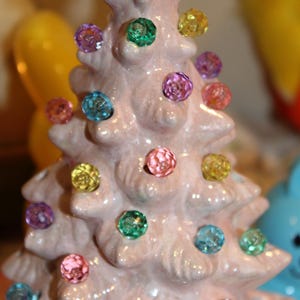 May include: A pink ceramic Christmas tree with colorful light bulbs. The tree is decorated with a variety of colors, including pink, blue, green, yellow, and purple.