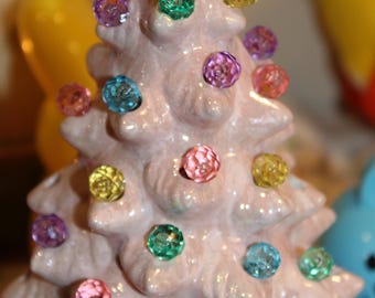 Puede incluir: Un árbol de Navidad de cerámica rosa decorado con bombillas de colores. El árbol está decorado con una variedad de colores, incluyendo rosa, azul, verde, amarillo y morado.