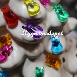 May include: A white ceramic Christmas tree decorated with colorful bunny-shaped ornaments. The ornaments are in shades of red, yellow, green, blue, purple, and pink.