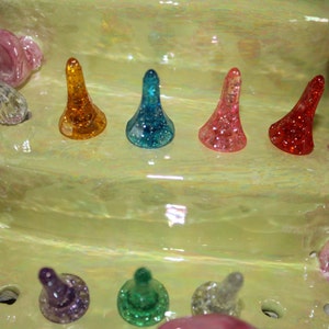May include: A close-up of a green ceramic Christmas tree with colorful glass ornaments. The ornaments are in the shape of a cone and are arranged in a row on the tree. The ornaments are red, orange, yellow, green, blue, and purple.