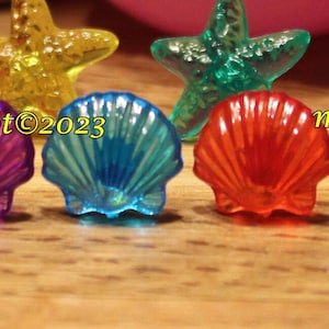 May include: Assortment of colorful plastic seashells and starfish ornaments. The shells are translucent and have a variety of colors, including pink, purple, blue, green, and yellow. The starfish are also translucent and have a variety of colors, including red, orange, and yellow.