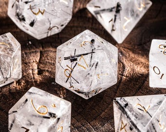 May include: Set of seven clear, gemstone dice with gold numbering and black inclusions. The dice are displayed in a wooden bowl, showcasing their multifaceted shapes and unique internal patterns. Ideal for tabletop games.