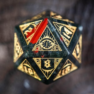 May include: A detailed close-up of a d20 die with a dark green and red speckled surface. The die features gold-colored numbers and intricate geometric designs, including an eye symbol within a triangle. The overall aesthetic is ornate and mystical.