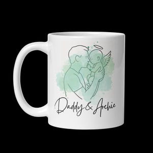 Puede incluir: Taza de cer&aacute;mica blanca con un dibujo lineal de un padre besando a un beb&eacute; &aacute;ngel. El dise&ntilde;o incluye un salpicado de acuarela verde y el texto "Daddy & Archie" en escritura cursiva.