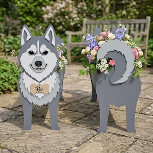 Puede incluir: Dos jardineras grises con forma de perro husky llenas de flores coloridas. La jardinera delantera tiene una etiqueta de madera que dice "Rex". Las jardineras son de madera y están diseñadas para contener plantas, agregando un toque decorativo a cualquier jardín o espacio al aire libre.
