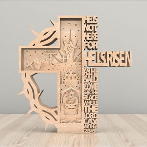 Puede incluir: Cruz de madera con intrincados diseños recortados. Presenta una corona de espinas, escenas bíblicas y las palabras "He is Risen". El texto "Matthew 28:6" también es visible. La cruz está hecha de madera clara.