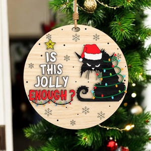May include: Wooden Christmas ornament with a black cat wearing a Santa hat and wrapped in Christmas lights. The text "IS THIS JOLLY ENOUGH?" is displayed on the ornament, along with snowflakes and a star.