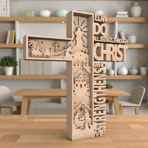 May include: A wooden cross with intricate cutouts depicting religious scenes and the text "I CAN DO ALL THINGS THROUGH CHRIST WHO STRENGTHENS ME." The cross is light brown and stands on a wooden surface.