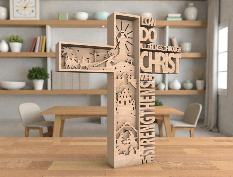 May include: A wooden cross with intricate cutouts depicting religious scenes and the text "I CAN DO ALL THINGS THROUGH CHRIST WHO STRENGTHENS ME." The cross is light brown and stands on a wooden surface.