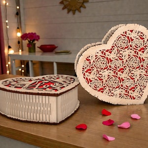 May include: Two heart-shaped wooden boxes with intricate rose cutouts. One box is open, revealing a red interior. The other box is closed. Scattered around are red and pink rose petals. The boxes are on a wooden surface.