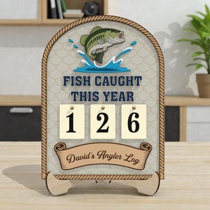 May include: Wooden fishing log with a fish jumping out of the water graphic. The text "FISH CAUGHT THIS YEAR" is above the numbers "126". The bottom banner reads "David's Angler Log". The frame has a rope design.