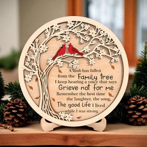 May include: A round wooden memorial plaque featuring a tree design with two red cardinals perched on a branch. The plaque includes the text "A limb has fallen from the Family tree...Grieve not for me...The good Life I lived." The plaque is supported by a wooden stand.