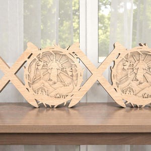 Puede incluir: Arte de pared decorativo de madera con un diseño de X y O. Las O son circulares, con un diseño en capas que representa un paisaje con un edificio, árboles y un sol. El arte está hecho de madera de color claro y se encuentra sobre una mesa de madera. Medidas en centímetros.