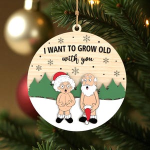 May include: Wooden Christmas ornament with the text "I WANT TO GROW OLD with you". The ornament features a cartoon illustration of an elderly couple, with a Santa hat and snowflakes. The ornament is hanging on a Christmas tree.