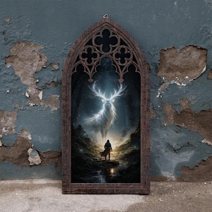 May include: A dark brown wooden frame with a pointed gothic arch top containing a print of a glowing white stag in a dark forest. A small figure stands in the foreground holding a lantern, facing the large, luminous, antlered creature.