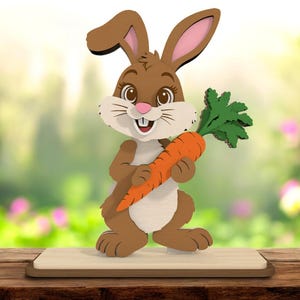Puede incluir: Una figura de conejo de Pascua de madera, sosteniendo una zanahoria naranja brillante con hojas verdes. El conejo es marrón y blanco con el interior de las orejas rosado y una cara sonriente. La figura está sobre una base de madera, sobre un fondo verde y rosa borroso.