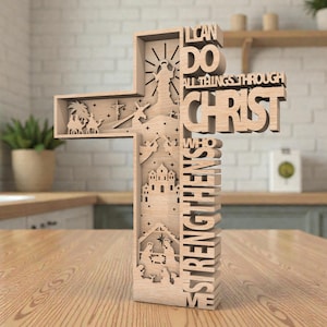 May include: A wooden cross with the words "I CAN DO ALL THINGS THROUGH CHRIST WHO STRENGTHENS ME." The cross features cut-out images of religious scenes, including a nativity scene and a figure with outstretched arms.