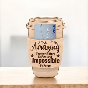May include: A wooden coffee cup-shaped holder with a sleeve that reads "A Truly Amazing Teacher Is Hard To Find And Impossible To Forget." A blue credit card is inside. The holder is on a wooden surface.