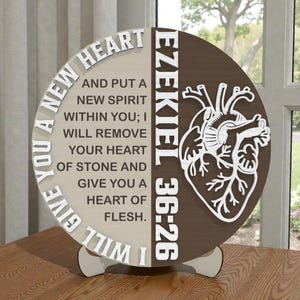 May include: A two-toned wooden decorative piece with a heart-shaped anatomical design. The left side features the text "I WILL GIVE YOU A NEW HEART" and a Bible verse. The right side has the text "EZEKIEL 36:26".