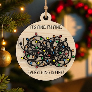 May include: Wooden Christmas ornament with the text "IT'S FINE. I'M FINE. EVERYTHING IS FINE!" featuring a tangled string of colorful Christmas lights and a power outlet. The ornament is hanging from a natural twine string.