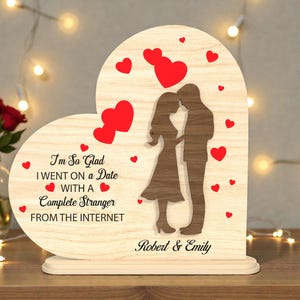 Può includere: Targa a forma di cuore in legno con la silhouette di una coppia che si abbraccia. La targa presenta cuori rossi e il testo "I'm So Glad I went on a Date with a Complete Stranger from the Internet" e i nomi "Robert & Emily".